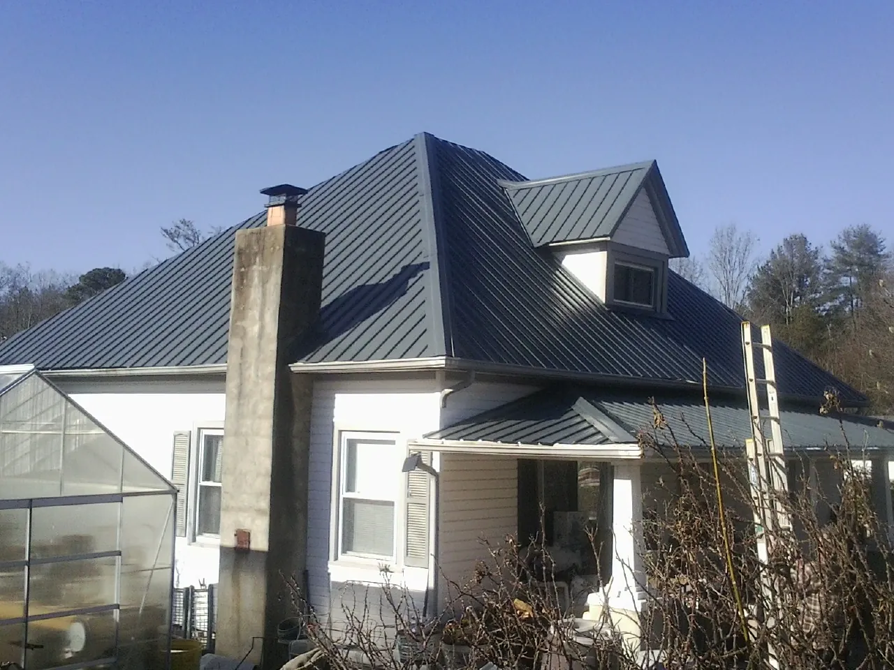 Dark blue standing seam metal roof on a white farmhouse with dormer — Slate & Tile Roof Repair by Roofing Brothers in Medina