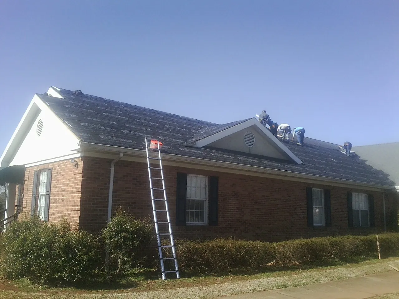 Crew tearing shingles off a brick ranch roof with a ladder set — Metal Roof Repair work by our crew in Medina