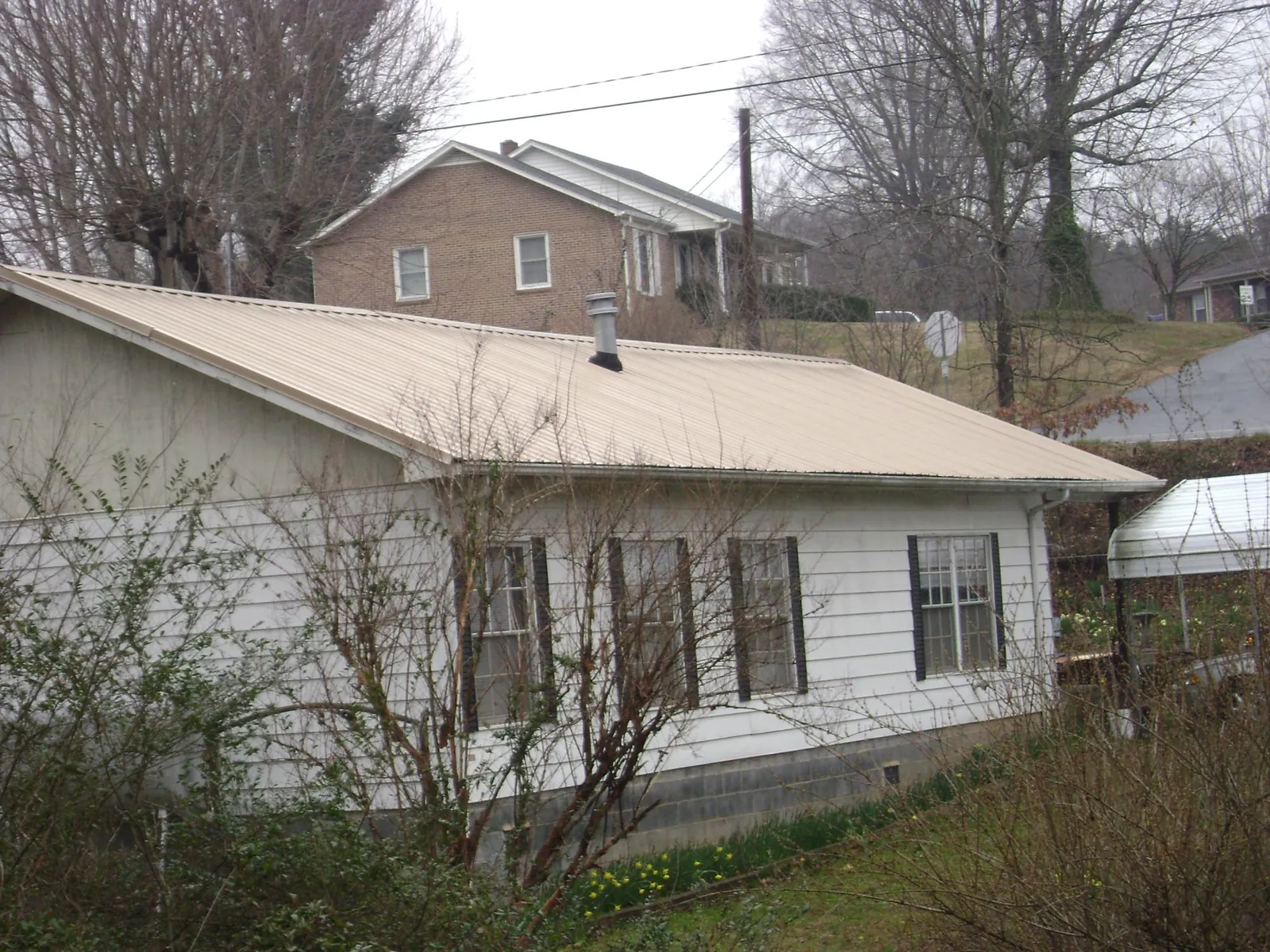 Tan metal roof on a white sided house set into a hillside — Commercial Roofing by Roofing Brothers in Medina